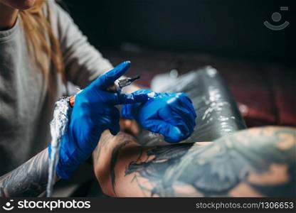 Female tattooist makes tattoo by machine on the shoulder. Professional tattooing in salon. Tattooist makes tattoo by machine on male shoulder