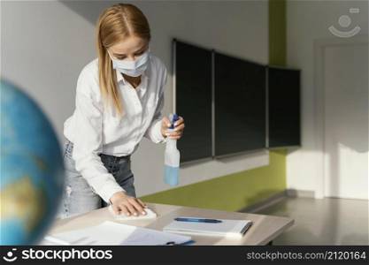 female teacher disinfecting her desk classroom
