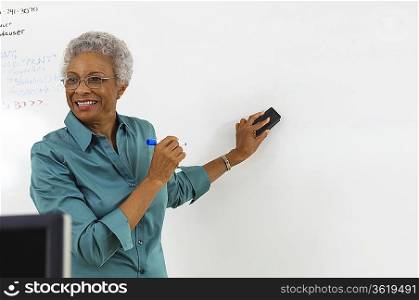 Female teacher erasing text on whiteboard in classroom