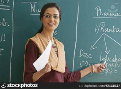 Female teacher explaining a lesson while standing against chalkboard