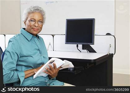 Female teacher holding book in computer classroom, portrait