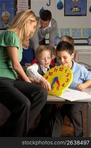 Female Teacher In Primary School Teaching Children To Tell Time In Classroom