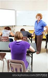 Female teacher monitoring a test in high school setting.