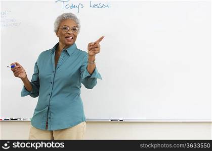 Female teacher pointing by whiteboard in classroom