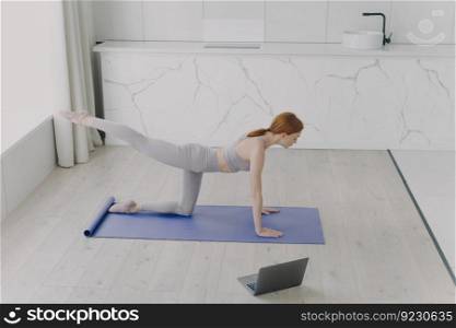 Female teacher shows workout on the online lesson. Young adult european woman is doing plank exercise. Sporty red haired girl practicing yoga in living room. Concept of e-learning and home classes.. Teacher shows workout on the online lesson. Young adult european woman is doing plank exercise