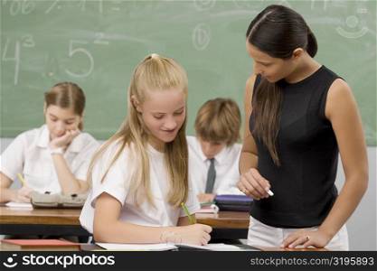 Female teacher teaching a schoolgirl with other students sitting in the background
