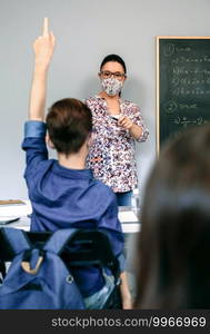 Female teacher with face mask in math class with student raising hand