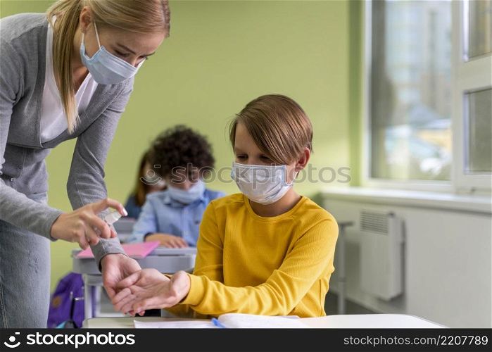 female teacher with medical mask giving hand sanitizer children class