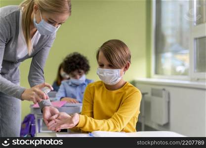 female teacher with medical mask giving hand sanitizer children class