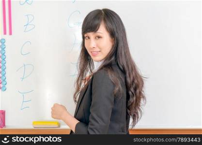 Female teacher writing ABCs on whoteboard looking at camera