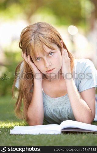 Female Teenage Student Studying In Park Looking Puzzled