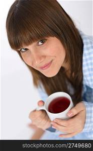 Female teenager in pajamas with cup of tea for breakfast