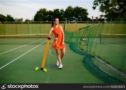 Female tennis player in sportswear poses at the net on outdoor court. Active healthy lifestyle, sport game competition, fitness training with racquet. Female tennis player in sportswear poses at net