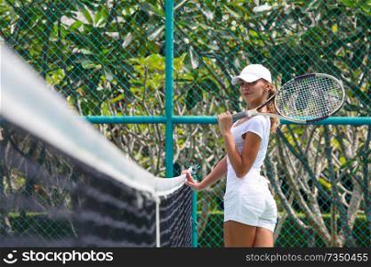 Female tennis player in white at tropical resort court. Female tennis player