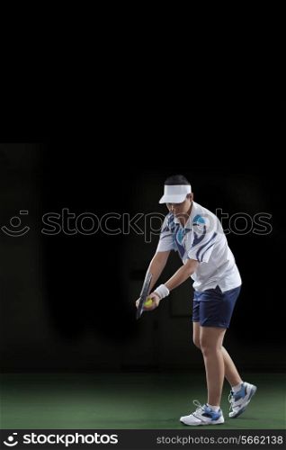Female tennis player preparing to serve over black background