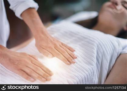 Female therapist performing Reiki therapy treatment holding hands over woman?s stomach. Alternative therapy concept of stress reduction and relaxation.