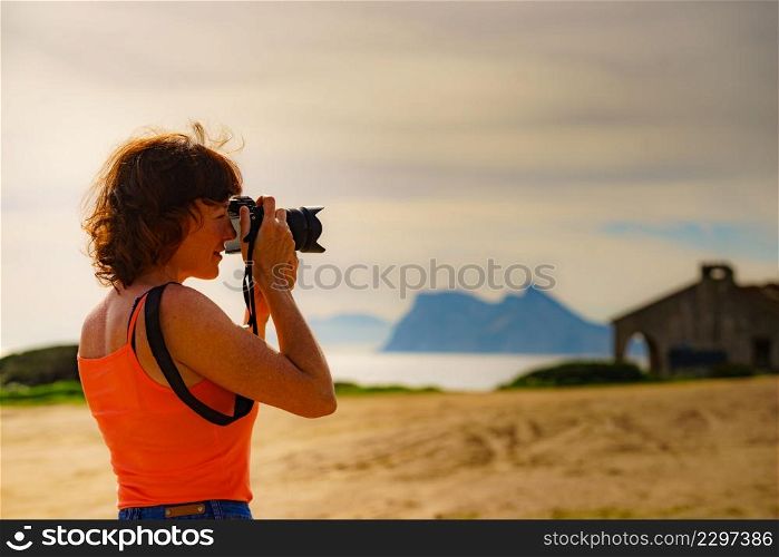 Female tourist on holidays taking photos with camera. Gibraltar rock on horizon. Torrecarbonera beach, Punta Mala, Andalusia Spain.. Tourist with camera on spanish coast.