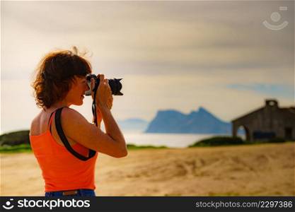 Female tourist on holidays taking photos with camera. Gibraltar rock on horizon. Torrecarbonera beach, Punta Mala, Andalusia Spain.. Tourist with camera on spanish coast.