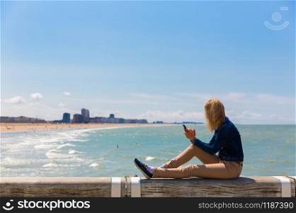 Female tourist sitting on pier on city beach, sea coast, Europe. Summer tourism and travels, famous and popular places for vacation tour or holidays. Female tourist sitting on pier, city beach, Europe