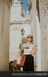 Female tourist with a paper city map on narrow streets of Ostuni, Italy