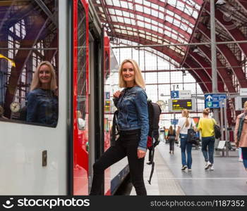 Female tourist with backpack enters the train on railway station platform, travel in Europe. Transportation by european railroads, comfortable tourism and travelling