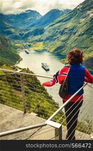 Female tourist with norwegian flag enjoying scenic view over fjord Geirangerfjord with cruise ship. Cruising vacation and travel.. Tourist over Geirangerfjord with norwegian flag