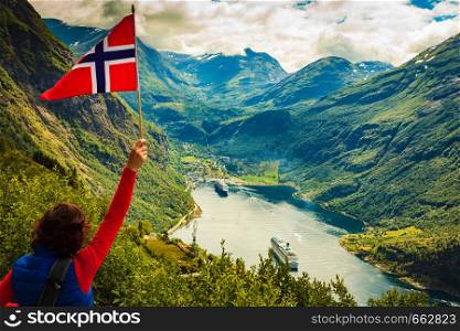 Female tourist with norwegian flag enjoying scenic view over fjord Geirangerfjord with cruise ship. Cruising vacation and travel.. Tourist over Geirangerfjord with norwegian flag