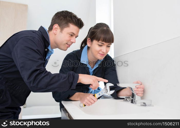 Female Trainee Plumber Working On Tap In Bathroom