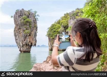 Female traveler he is taking photo a beautiful natural scenery by cell phone at Khao Tapu or James Bond Island in Ao Phang Nga Bay National Park, Thailand