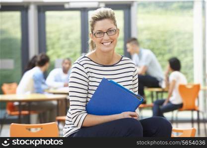 Female Tutor Sitting In Classroom With Folder