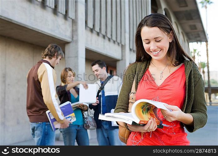 Female university student holding book, outdoors