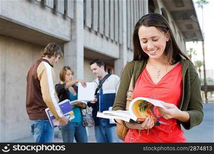 Female university student holding book, outdoors