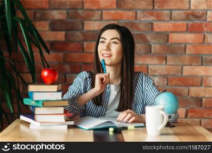 Female university student sitting at the table with textbooks and apple on the top, brick wall on background, knowledge concept. Female student sitting at the table with textbooks
