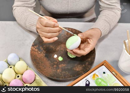 Female using a brush to paint an egg with a brush, surrounded by painted eggs and tools. Selective focus. Easter holidays and artistic concept.