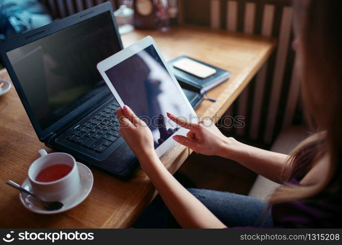Female using tablet pc in cafe, laptop and cell phone on wooden table.