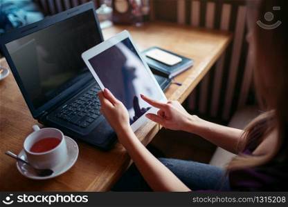 Female using tablet pc in cafe, laptop and cell phone on wooden table.