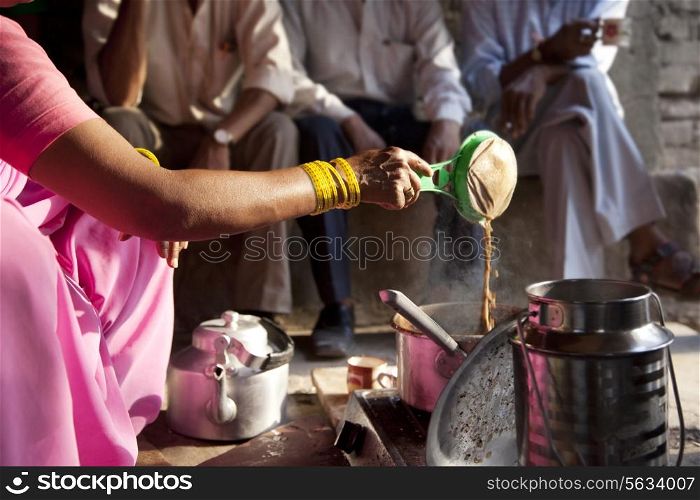 Female vendor preparing chai with customers sitting in background
