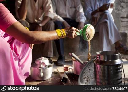 Female vendor preparing chai with customers sitting in background