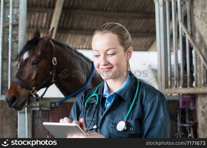 Female Vet With Digital Tablet Examining Horse In Stable