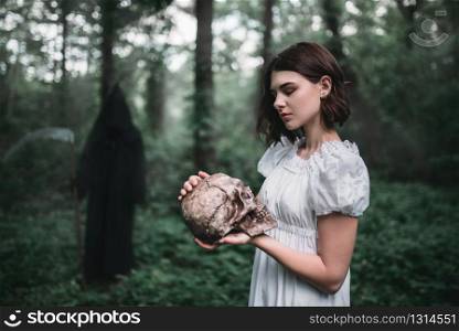 Female victim in white dress holds human skull in hands in the forest and death. Photo in horror style. Victim holds human skull, death on background
