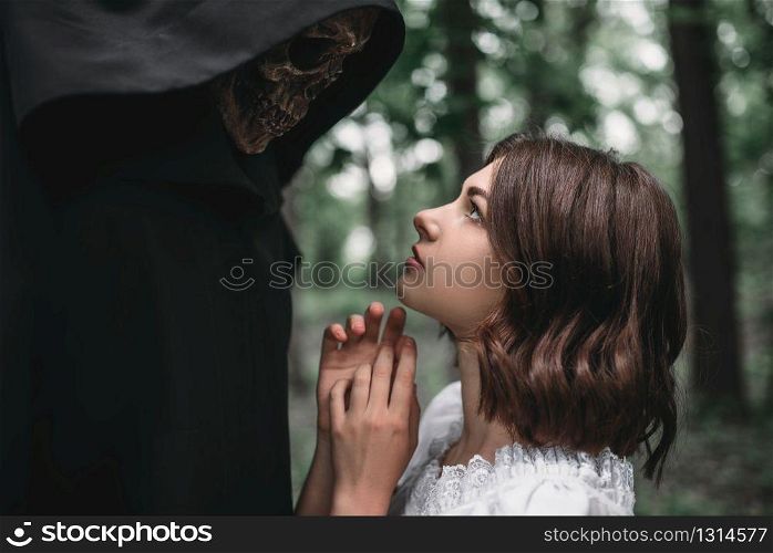 Female victim looks into the eyes of death in a black hoodie, forest on background. Photo in horror style, mystery ritual. Female victim looks into the eyes of death