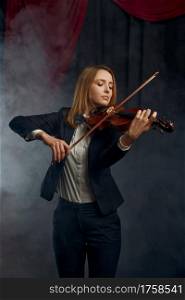 Female violonist with bow and violin, performance on stage. Woman with string musical instrument, music art, musician play on viola, dark background. Female violonist with violin, performance on stage