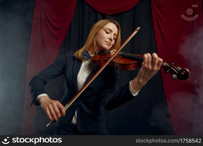 Female violonist with bow and violin, performance on stage. Woman with string musical instrument, music art, musician play on viola, dark background. Female violonist with violin, performance on stage