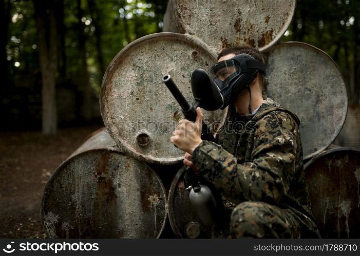 Female warrior in camouflage and protection mask holds paintball gun. Extreme sport with pneumatic weapon and paint bullets or markers, military team game outdoors, combat tactics. Female warrior in camouflage holds paintball gun