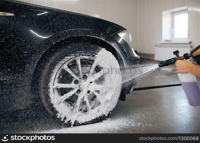 Female washer applies foam to the wheel, car wash. Woman cleans vehicle, carwash station, car-wash business