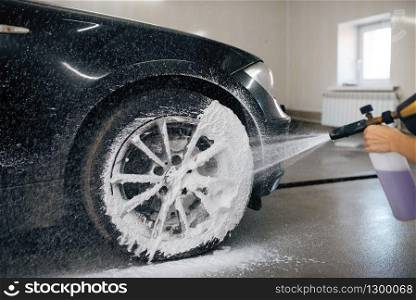 Female washer applies foam to the wheel, car wash. Woman cleans vehicle, carwash station, car-wash business