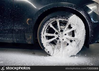 Female washer applies foam to the wheel, car wash. Woman cleans vehicle, carwash station, car-wash business. Female washer applies foam to the wheel, car wash