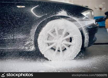 Female washer applies foam to the wheel, car wash. Woman cleans vehicle, carwash station, car wash. Female washer applies foam to the wheel, car wash
