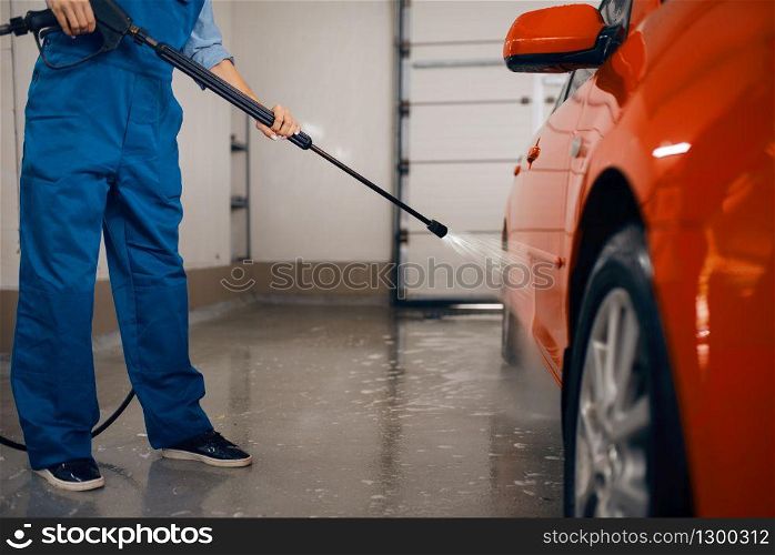 Female washer in uniform cleans the auto with high pressure gun in hands, car wash. Woman washes vehicle, carwash station, car wash business. Female washer with high pressure gun, car wash