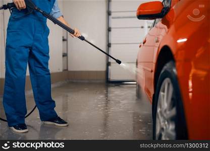 Female washer in uniform cleans the auto with high pressure gun in hands, car wash. Woman washes vehicle, carwash station, car wash business. Female washer with high pressure gun, car wash